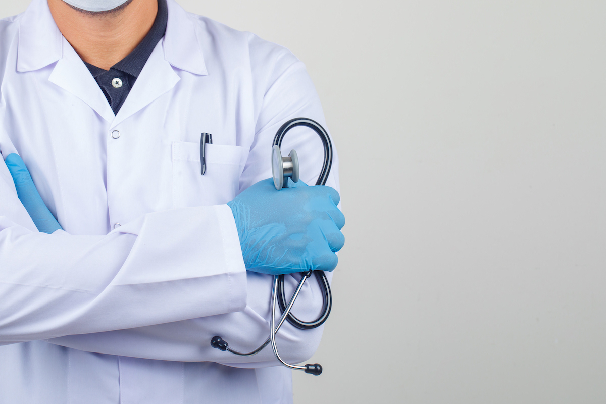 Doctor crossing arms while holding stethoscope in white coat front view.